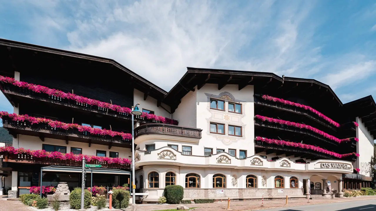 Traditionelles Hotel Das Walchsee Sportresort mit blühenden Balkonen und Alpenblick unter blauem Himmel.
