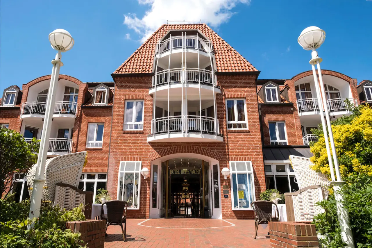 Eingangsbereich des Hotel Resort und Spa Hohe Wacht mit rotem Ziegeldach, Balkonen und Aussenbeleuchtung unter blauem Himmel.