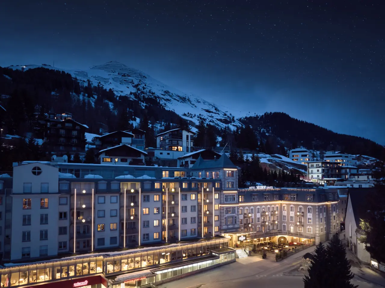 Beleuchtetes Precise Tale Seehof Davos Hotel bei Nacht, umgeben von verschneiten Bergen und klarem Sternenhimmel.