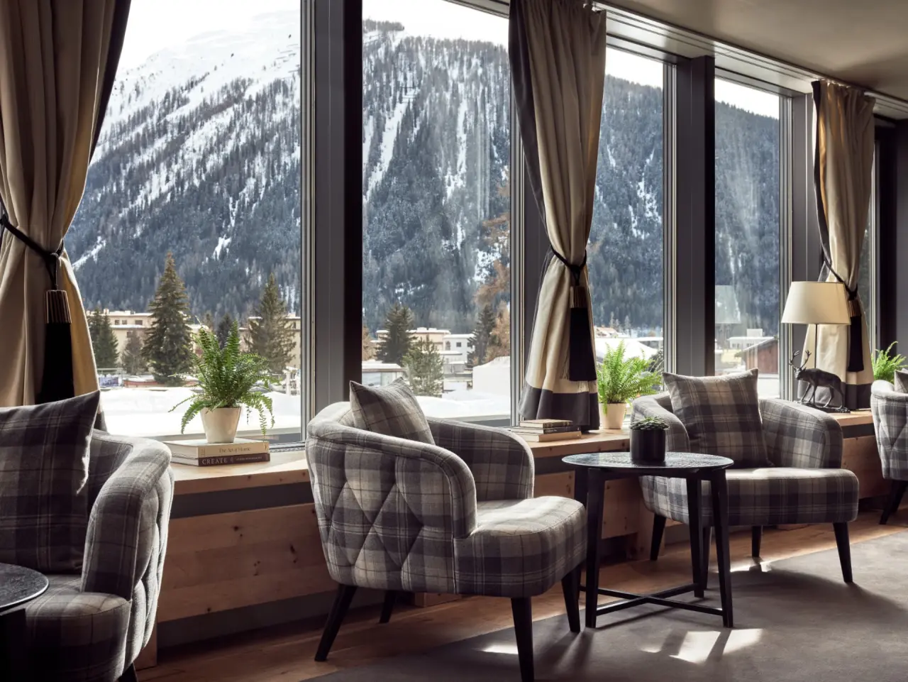 Gemütliche Lounge mit karierten Sesseln und Panoramablick auf die verschneiten Berge im Precise Tale Seehof Davos.
