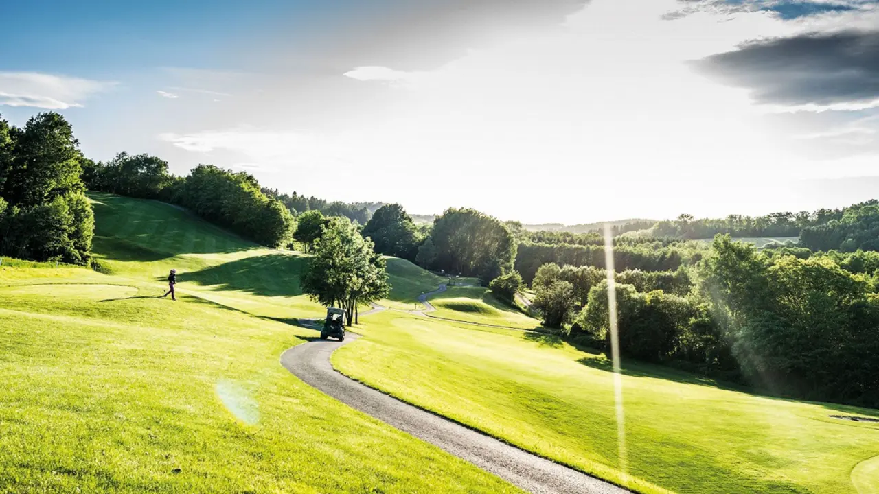 Sonnenverwöhnter Golfplatz des Allegria Resort Stegersbach mit Golfer und Golfcart. Grüne Hügellandschaft für Aktivurlaub.