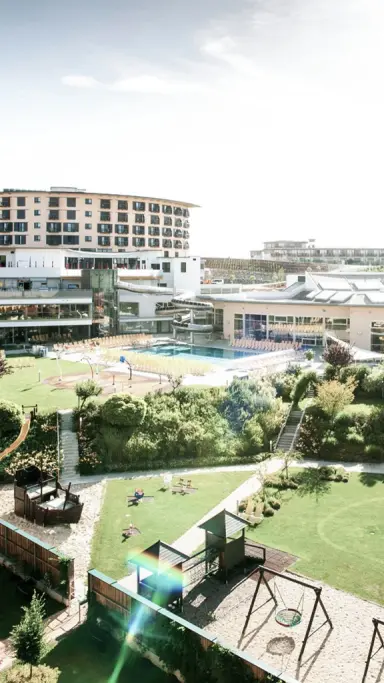 Luftaufnahme des Allegria Resort Stegersbach mit Hotelgebäude, großem Außenpool und weitläufigem Gartenbereich mit Spielplätzen.
