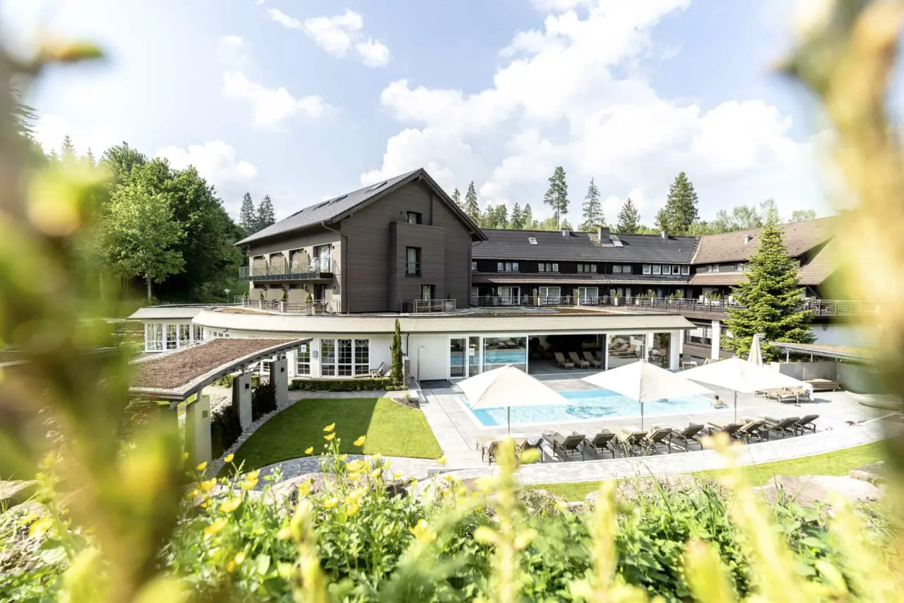 Panoramablick auf das Hotel Waldsägmühle mit grossem Aussenpool, Sonnenterrasse und umgebender Waldlandschaft.
