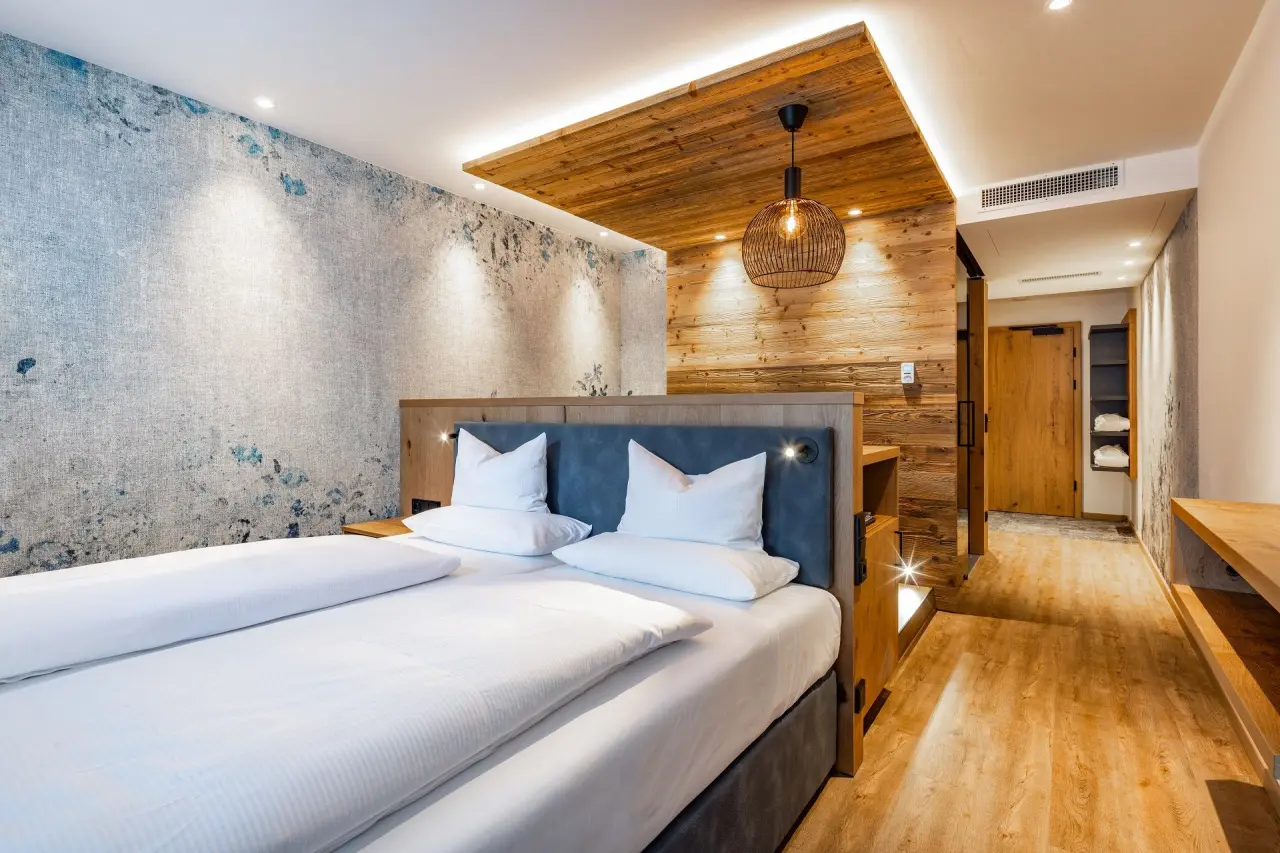 Modernes Doppelzimmer mit Holzelementen und gemütlichem Bett im Alm- & Wellnesshotel Alpenhof.