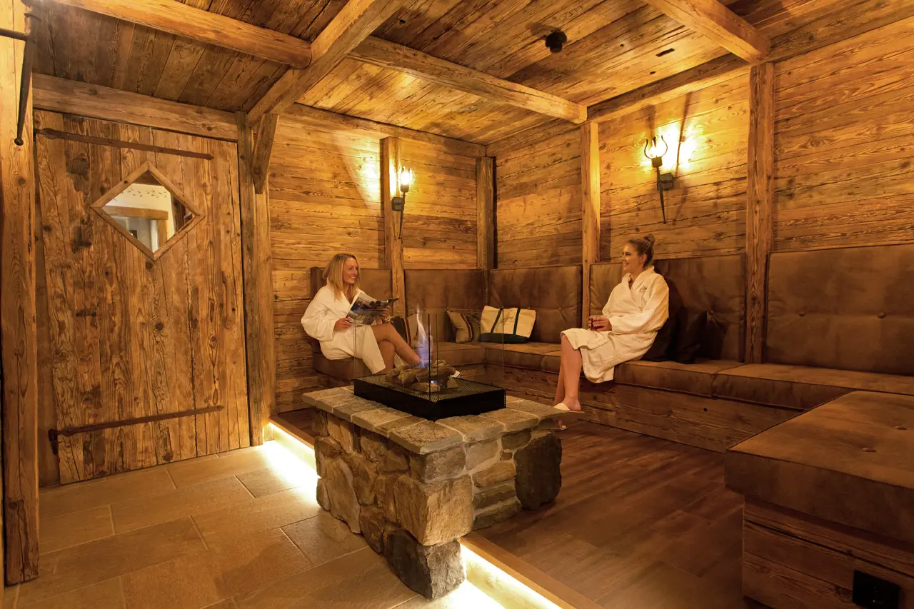 Gäste entspannen im gemütlichen Ruheraum mit Kamin im Spa-Bereich des Alm- & Wellnesshotel Alpenhof.