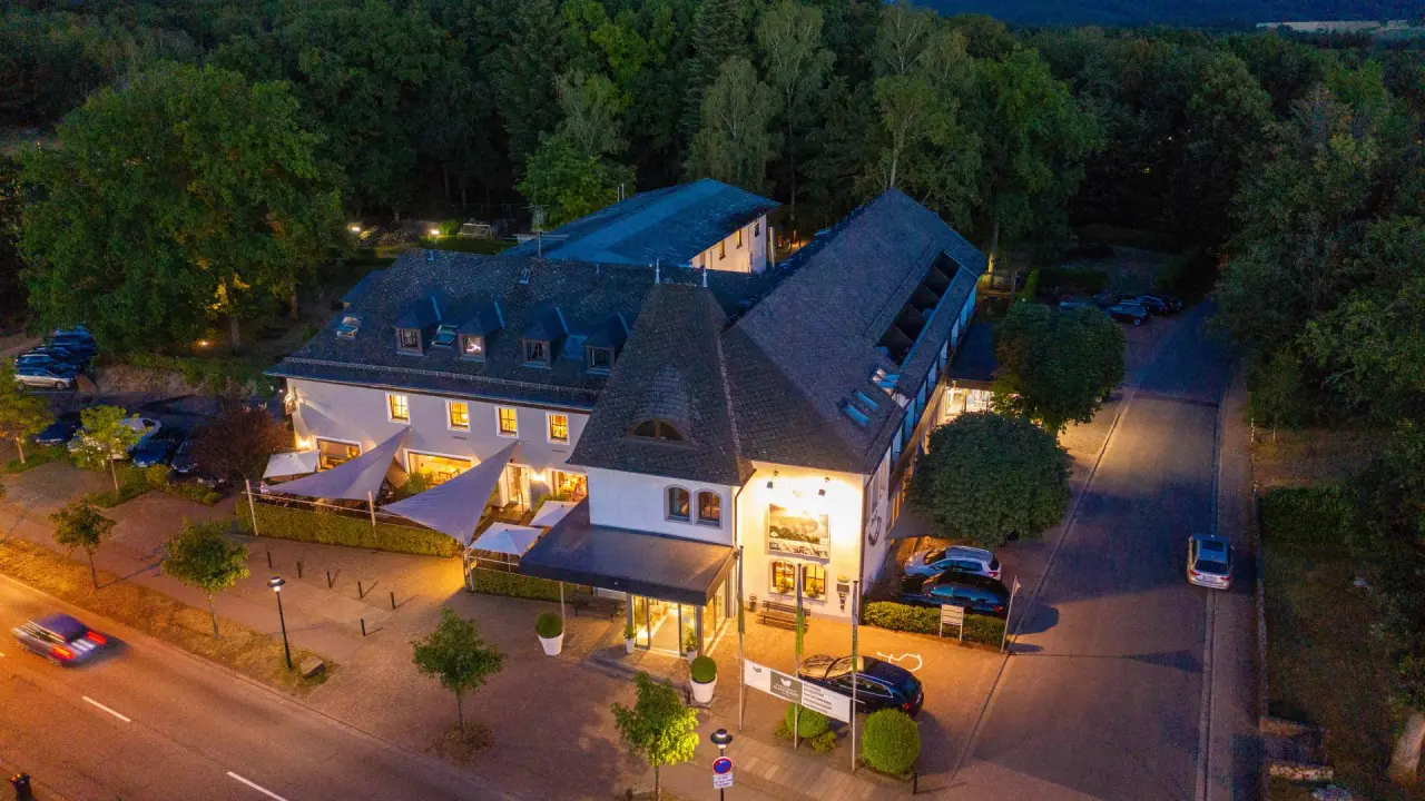 Beleuchtetes Buchnas Landhotel Saarschleife bei Nacht, eingebettet in grüne Natur, mit einladendem Aussenbereich.