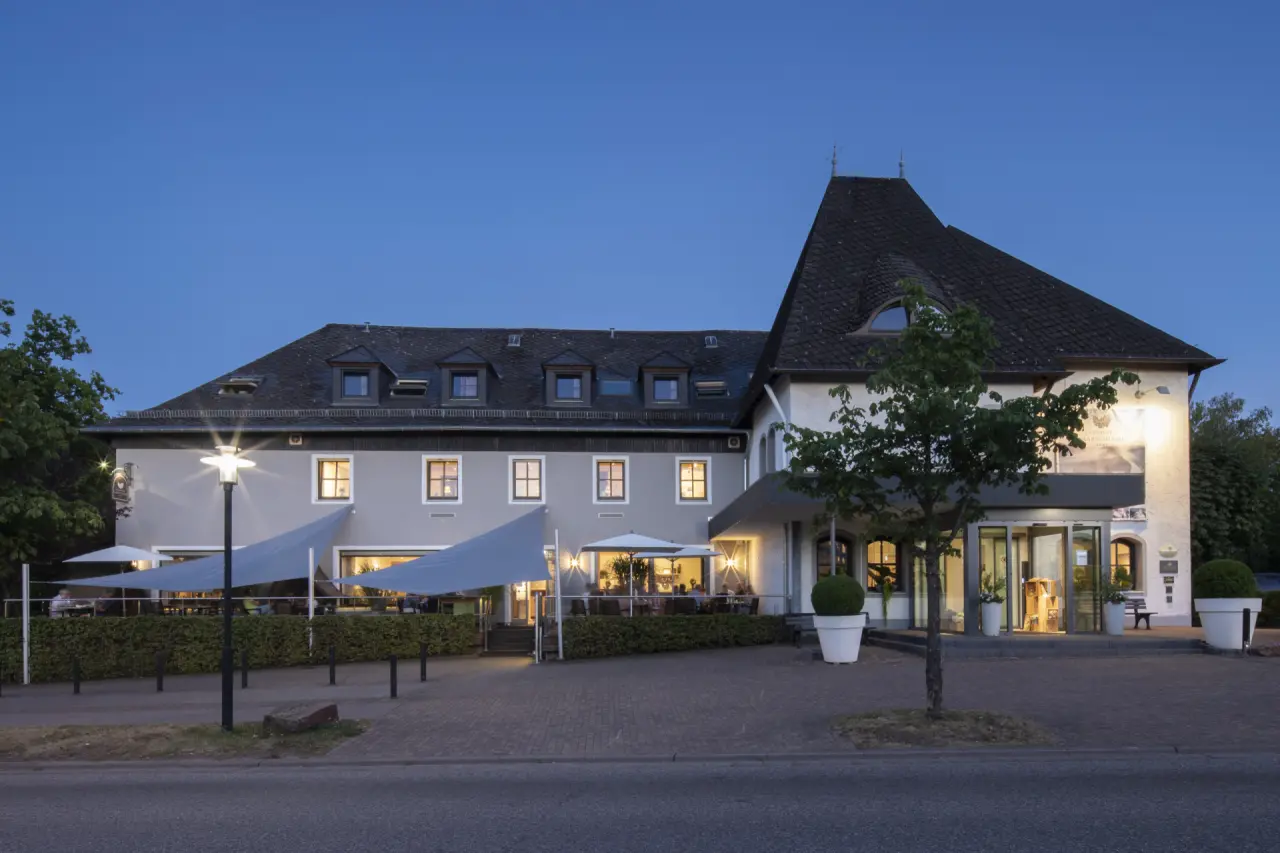 Aussenansicht von Buchnas Landhotel Saarschleife bei Abenddämmerung mit beleuchteter Terrasse und Eingang.