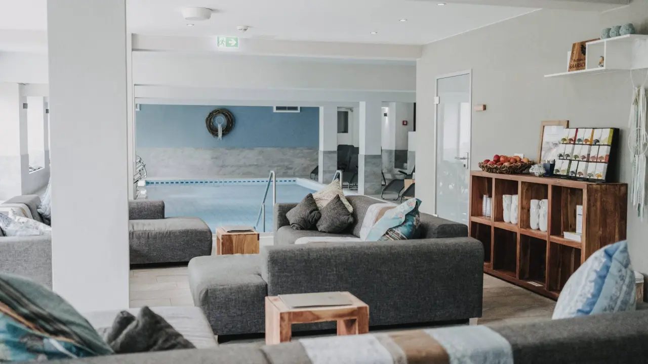 Entspannungsbereich mit bequemen Sofas und Blick auf den Innenpool im Buchnas Landhotel Saarschleife.