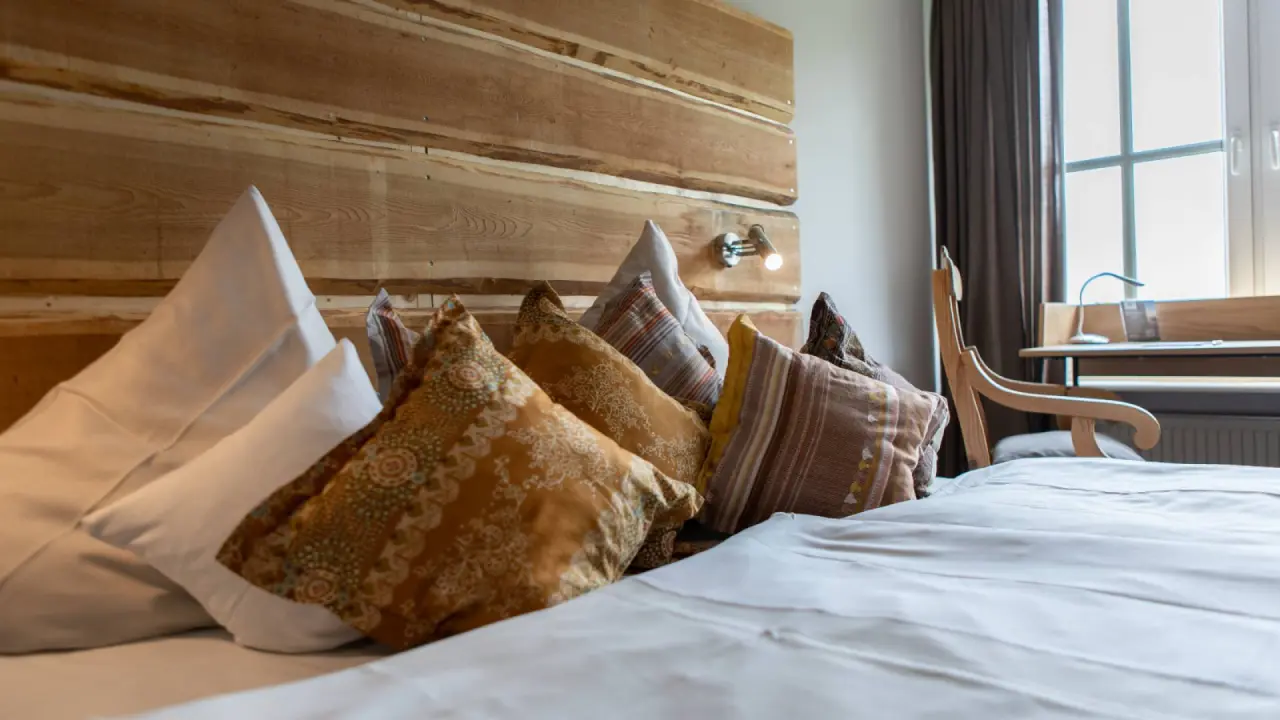 Gemütliches Doppelbett mit Holzkopfteil und bunten Kissen in einem Zimmer im Buchnas Landhotel Saarschleife.