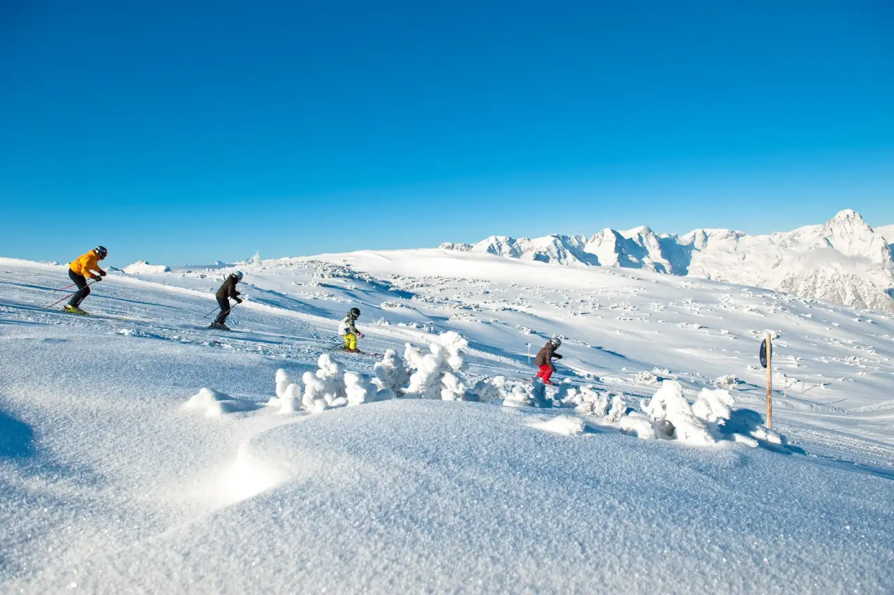 Skifahrer auf sonniger Piste mit verschneiten Bergen im Hintergrund, nahe IMLAUER Hotel Schloss Pichlarn.