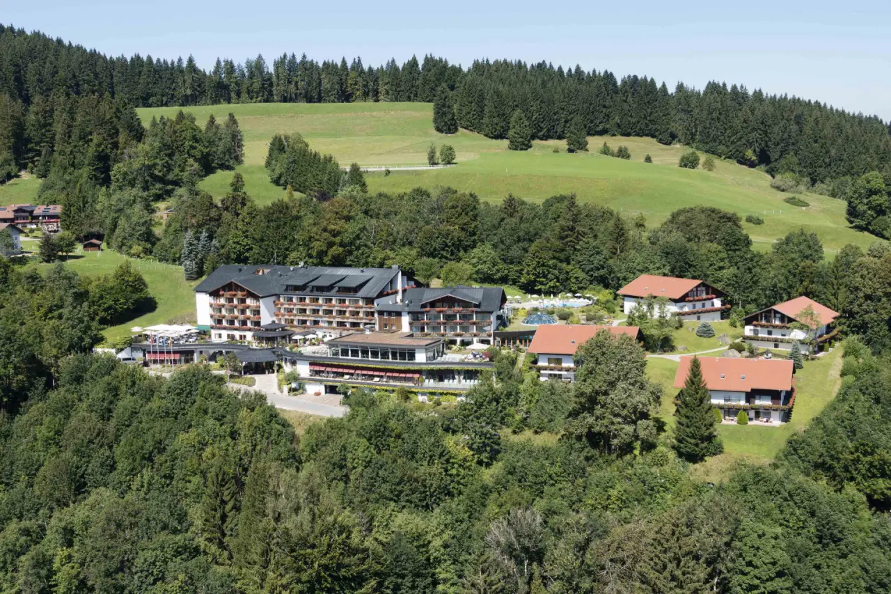 Luftaufnahme des 5* Sport- & Wellnesshotel Allgäu Sonne, eingebettet in grüne Hügel und Wälder mit Poolbereich.