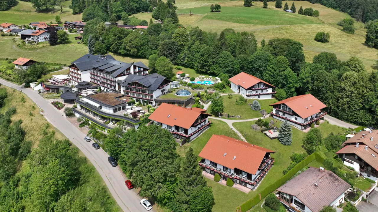 Luftaufnahme des 5* Sport- & Wellnesshotel Allgäu Sonne mit Aussenpool und grüner Hügellandschaft.