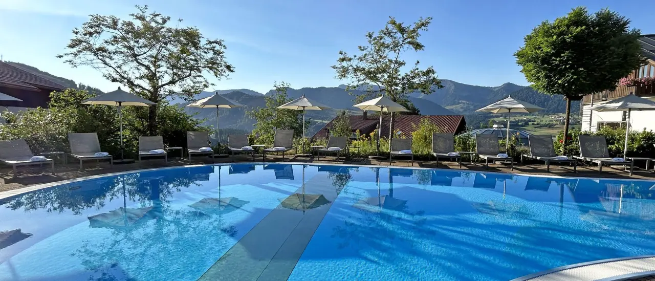 Aussenpool mit Sonnenterrasse und Liegestühlen vor malerischem Allgäuer Bergpanorama im 5* Sport- & Wellnesshotel Allgäu Sonne.