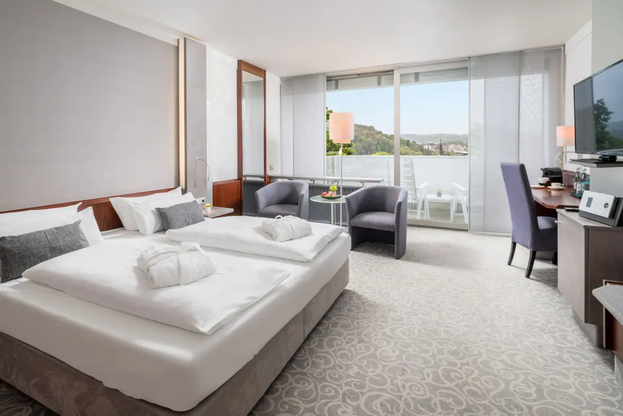 Helles Hotelzimmer im Hotel Frankenland mit Doppelbett, Sitzbereich, Schreibtisch und Balkon mit Ausblick ins Grüne.