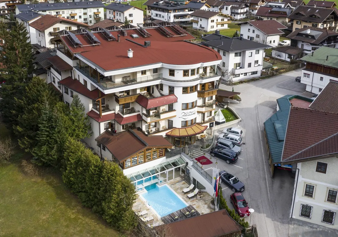 Luftaufnahme des Alpine Hideaway Zillertalerhof mit Aussenpool und rotem Dach in der Zillertaler Bergwelt.