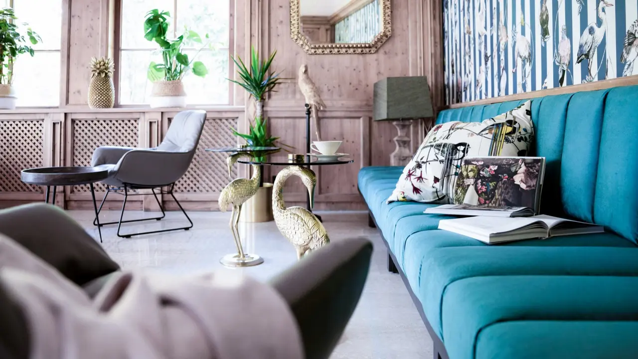 Stilvolle Lounge im Alpine Hideaway Zillertalerhof mit türkisfarbenem Sofa, Holzwänden und einzigartiger Dekoration.