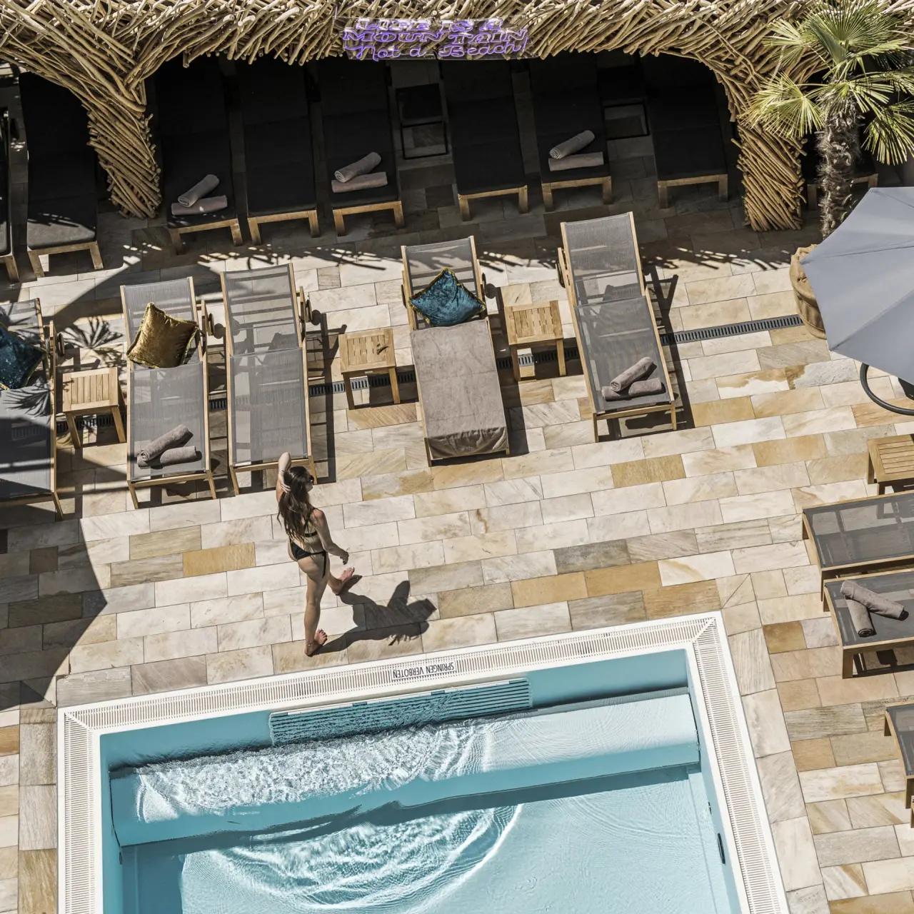 Blick von oben auf den Aussenpool mit Sonnenliegen und Palmen im Alpine Hideaway Zillertalerhof.