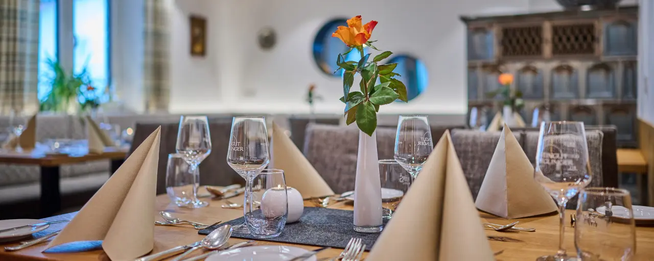 Einladend gedeckter Tisch mit frischer Rose und Weingläsern im Restaurant des Landhotel Geyer.
