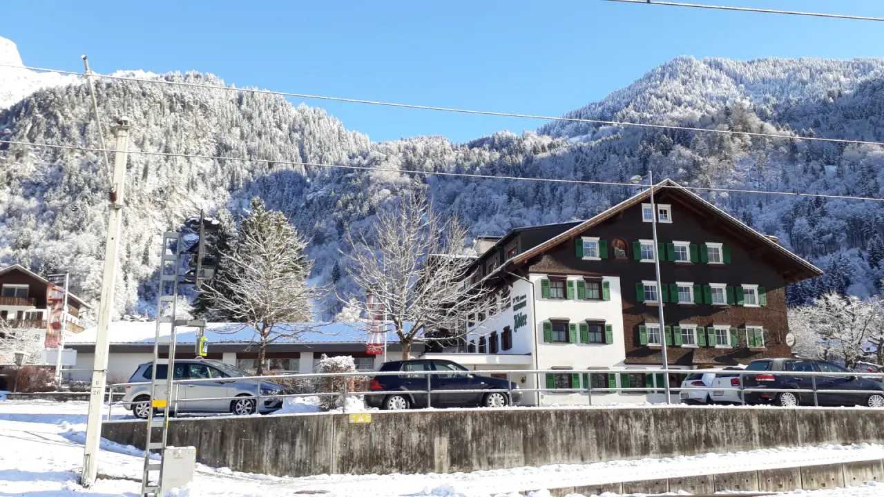 Winteransicht des Relax- & Vitalhotel Adler mit traditioneller Architektur vor verschneiter Berglandschaft und blauem Himmel.