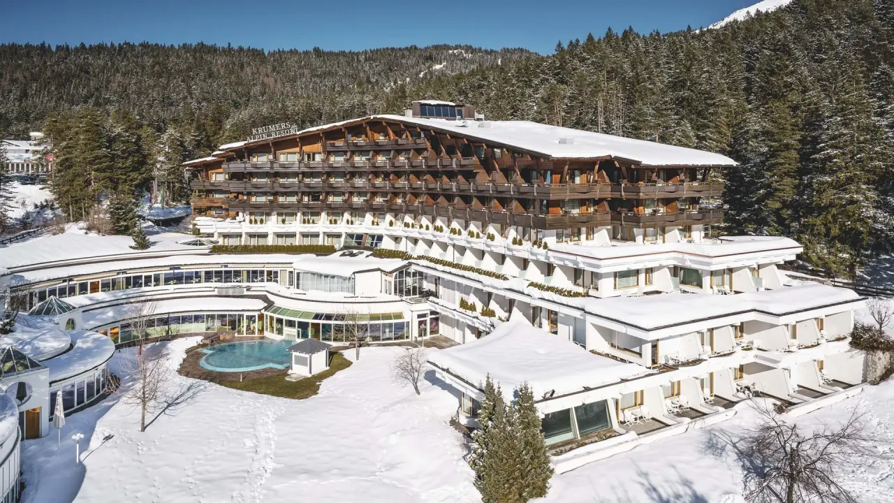 Krumers Alpin Resort im Winter: Panoramablick auf das Hotel mit verschneiter Berglandschaft und beheiztem Aussenpool.