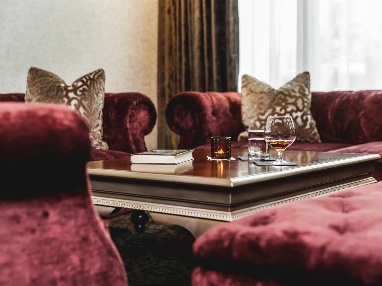 Gemütliche Lounge im Krumers Alpin Hotel mit Samtsofas, Holztisch, Buch und Getränken für entspannte Stunden.