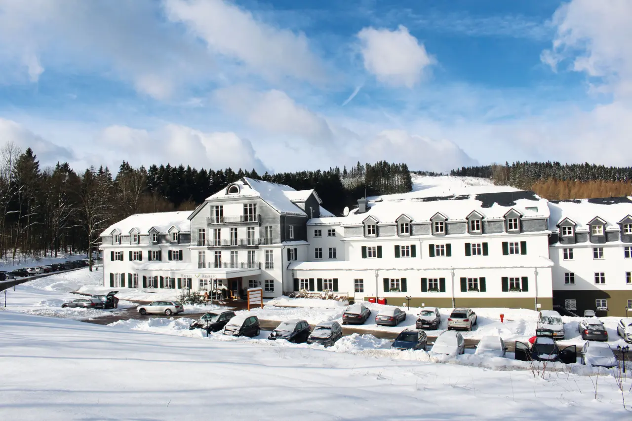 Winterliche Aussenansicht des Hotel Rimberg mit verschneiten Dächern und Wäldern unter blauem Himmel.