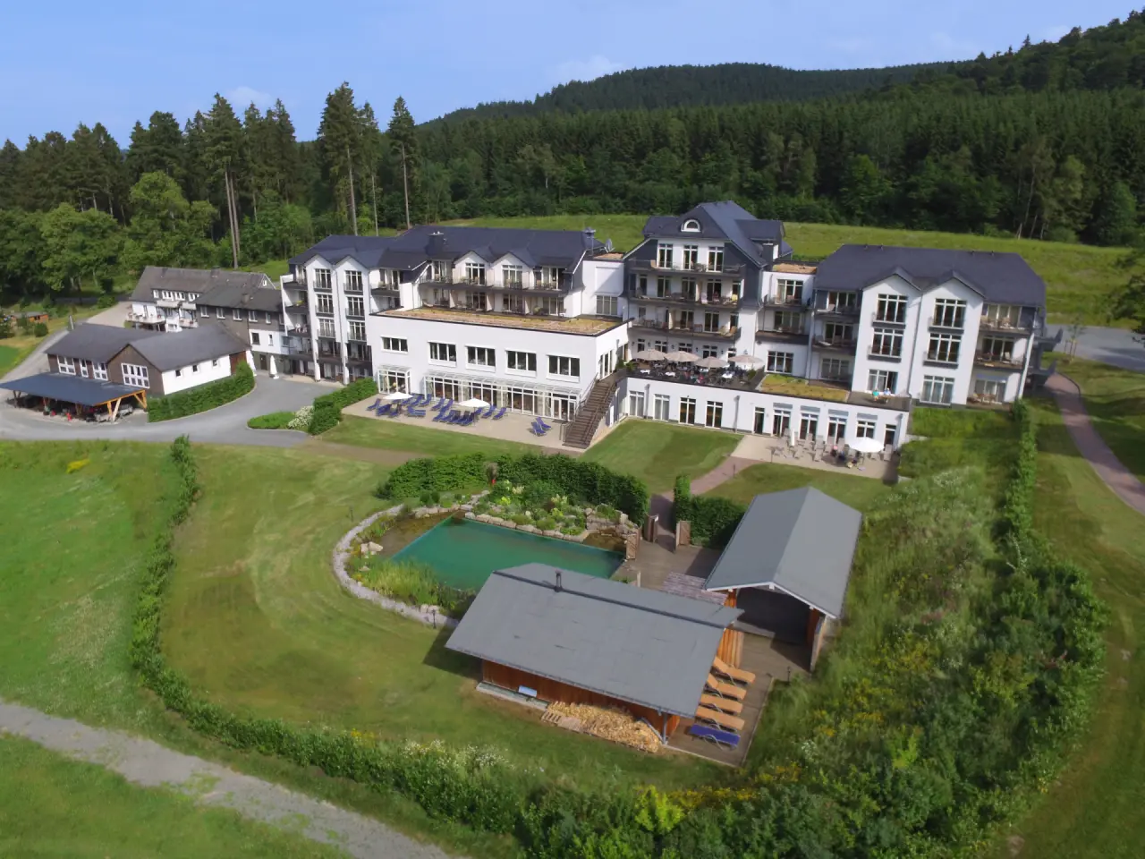 Luftaufnahme des Hotel Rimberg mit Aussenanlage, Naturpool und umliegendem Wald im Sauerland.