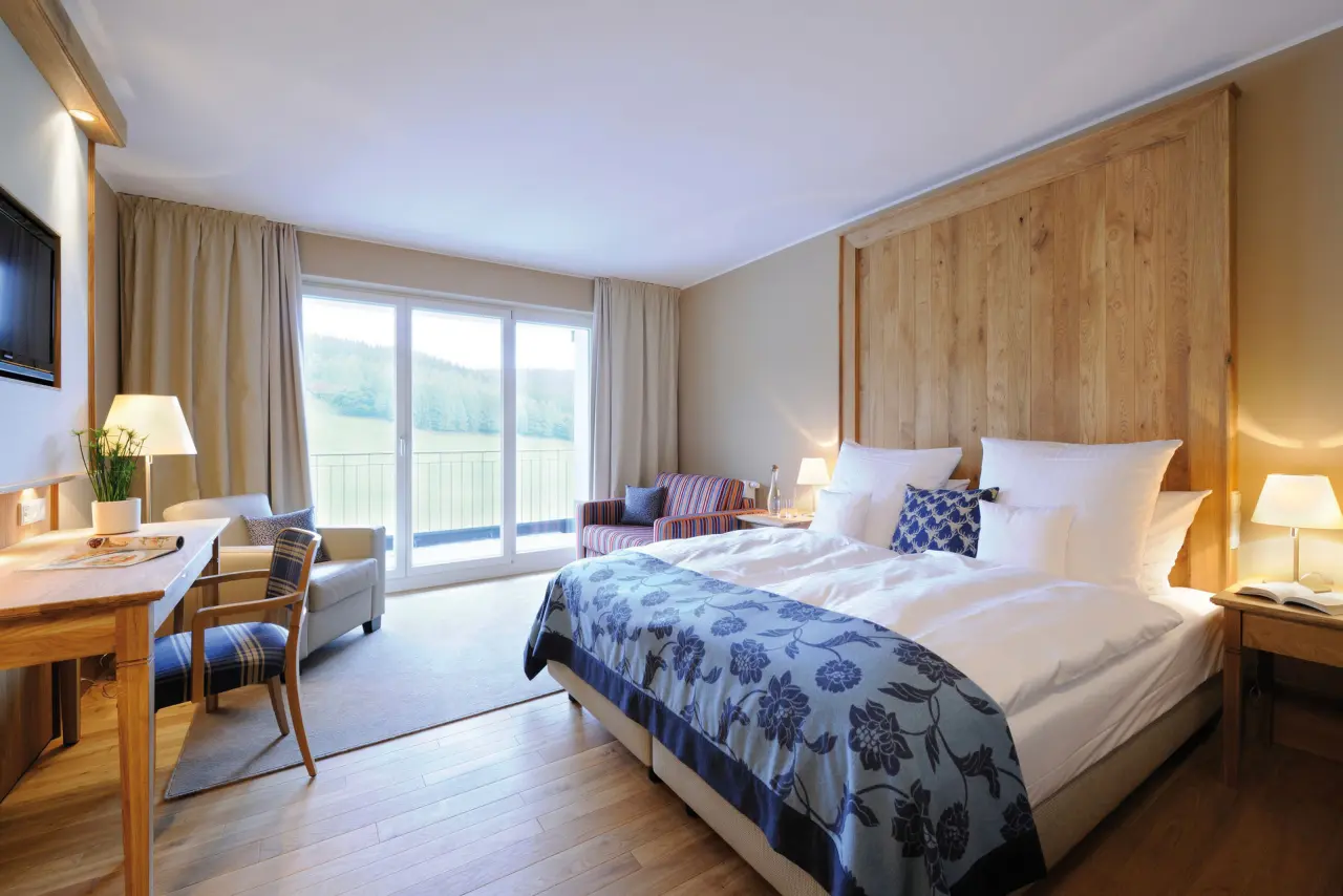 Helles, modernes Hotelzimmer im Hotel Rimberg mit Doppelbett, Sitzbereich und Balkon mit Blick auf die grüne Natur.