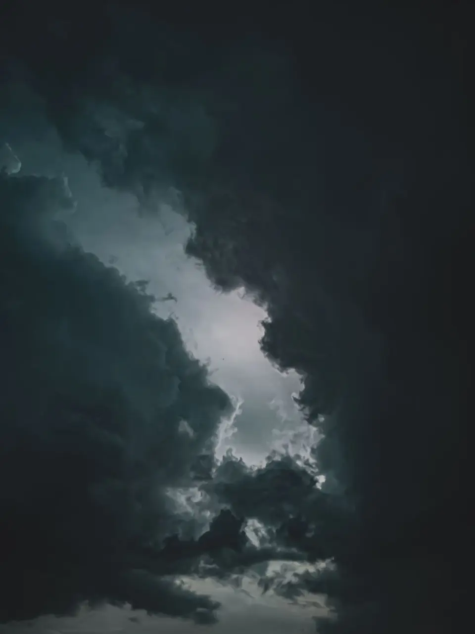 Dunkle, dramatische Wolkenformationen am Himmel mit einem hellen Durchbruch in der Mitte.