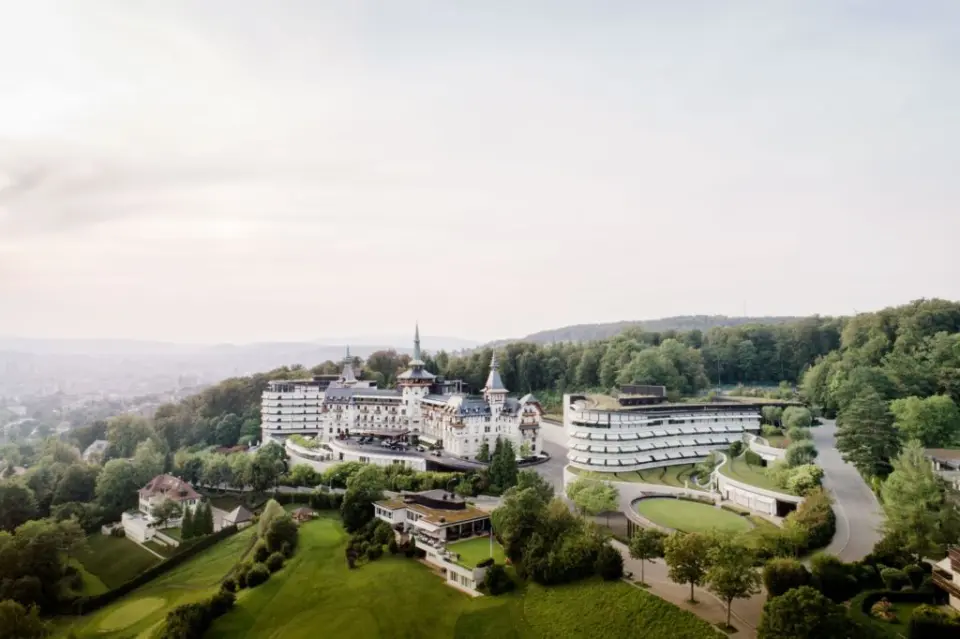 Majestätisches The Dolder Grand Hotel in Zürich, umgeben von grünen Hügeln und Wäldern, mit Blick auf die Stadt.