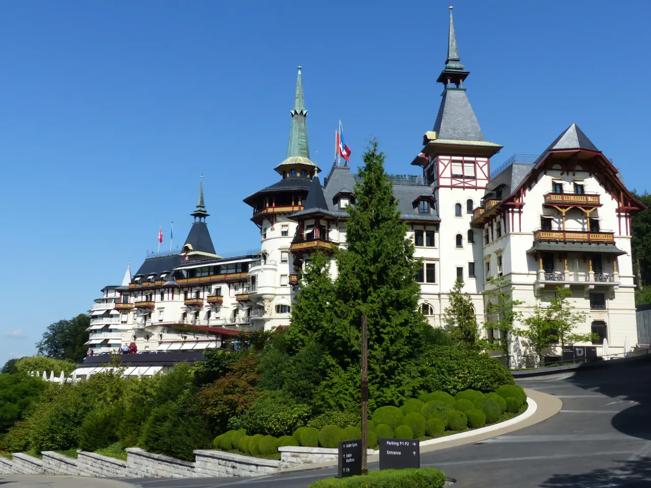 Aussenansicht des luxuriösen The Dolder Grand Hotels in Zürich mit markanten Türmen und grüner Umgebung unter blauem Himmel.