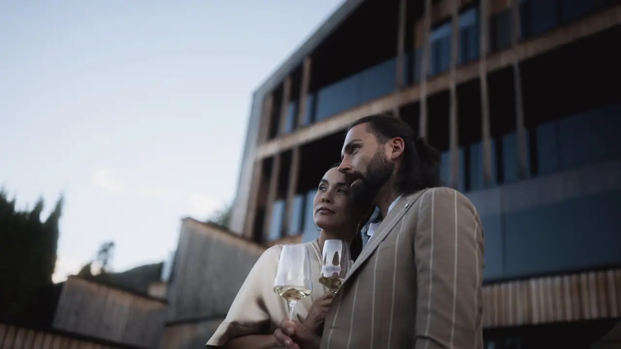 Hotel Winkler in St. Lorenzen – Paar mit Weingläsern vor der modernen Hotelfassade | Wellnesshotel Südtirol