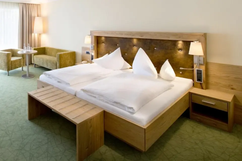 Komfortables Hotelzimmer im Parkhotel Bad Füssing mit Doppelbett, hellem Holz und gemütlichem Sitzbereich.