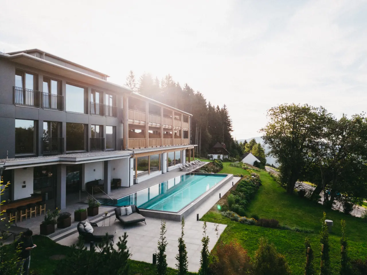 Aussenansicht des Naturhotel Bauernhofer mit langem Infinity-Pool, Sonnenterrasse und grüner Hügellandschaft bei Sonnenuntergang.