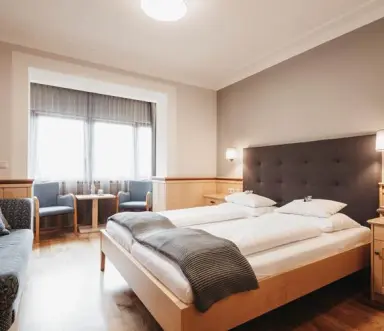 Helles, einladendes Doppelzimmer mit Holzboden und gemütlichem Sitzbereich im Naturhotel Bauernhofer für entspannte Nächte.