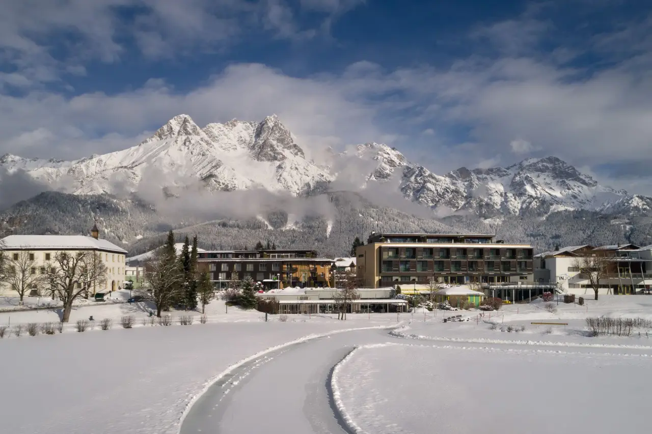 Winterlandschaft mit dem Ritzenhof Hotel & Spa am See, umgeben von verschneiten Bergen und einem zugefrorenen See.