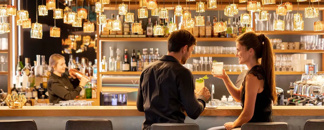 Gäste genießen Cocktails an der stilvollen Bar des Naturhotel Edelweiss mit moderner Beleuchtung und Barkeeper.