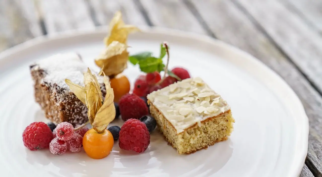 Zwei Stücke Kuchen mit frischen Beeren und Physalis auf einem Teller im Naturhotel Edelweiss.