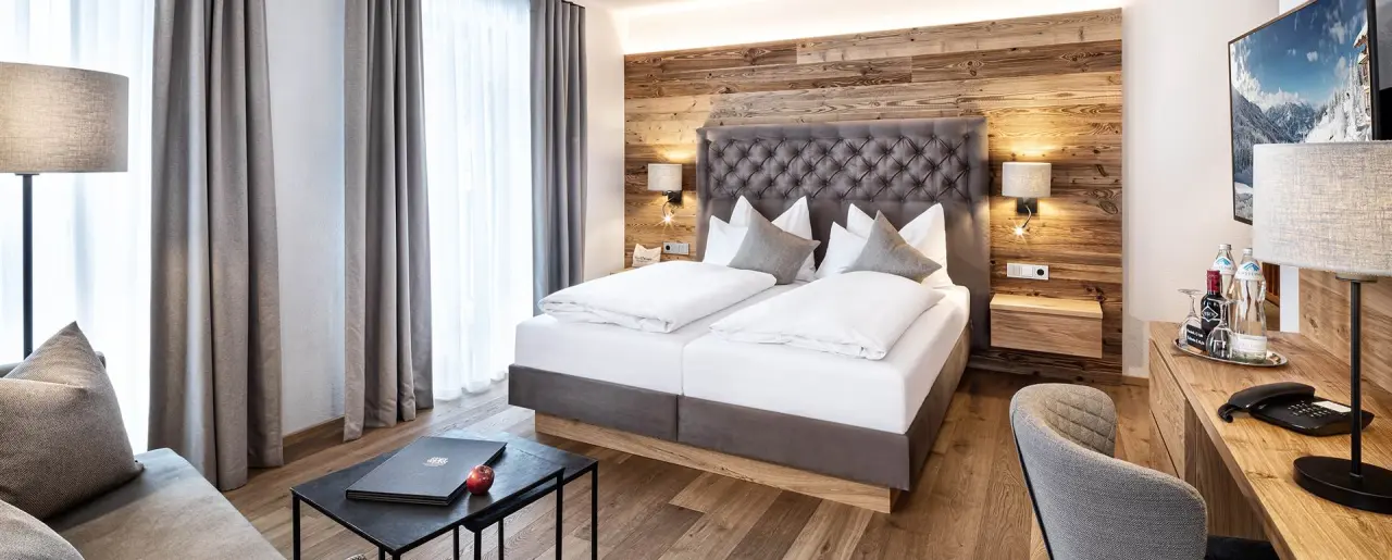 Modernes Doppelzimmer mit Holzwand, bequemen Betten und Sitzbereich im Naturhotel Edelweiss.