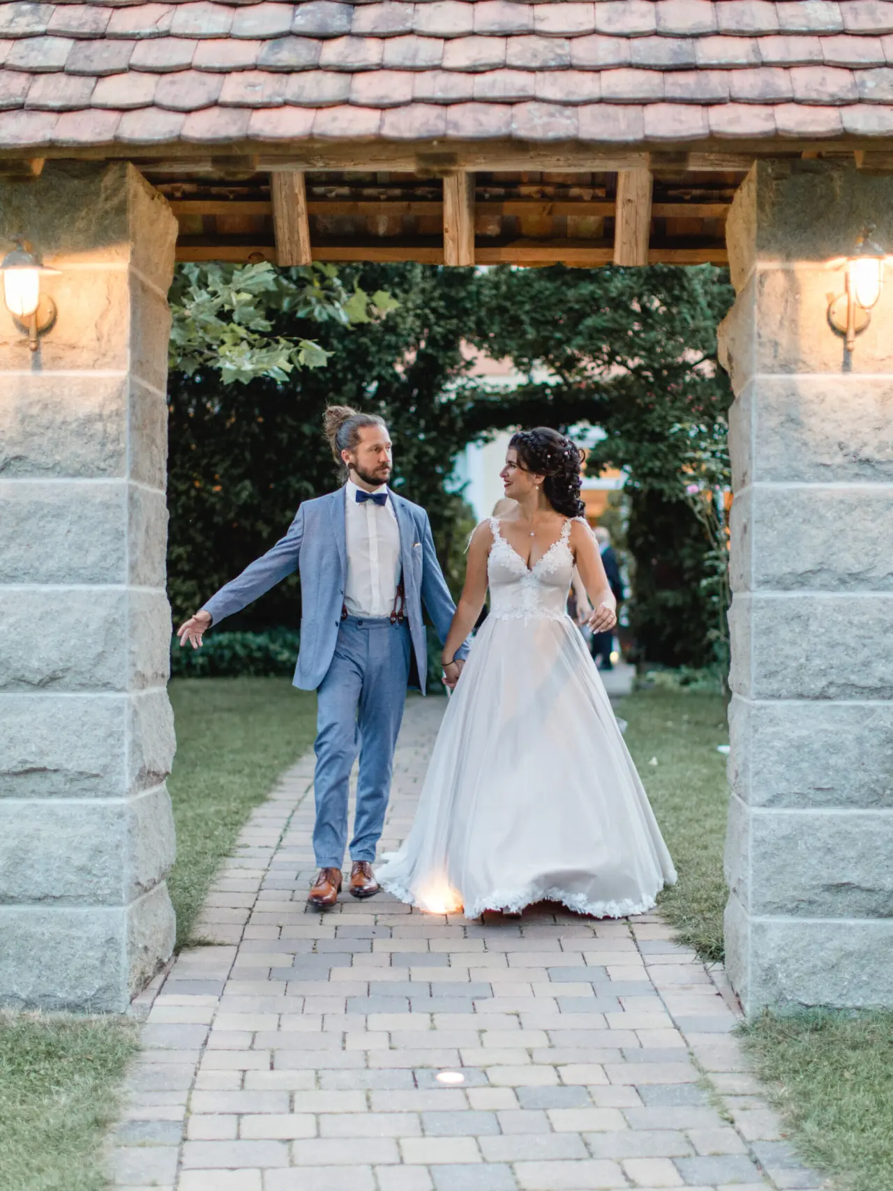 Hochzeitspaar im Gartenbereich des Meiser Vital Hotels unter einem beleuchteten Steinbogen am Abend.