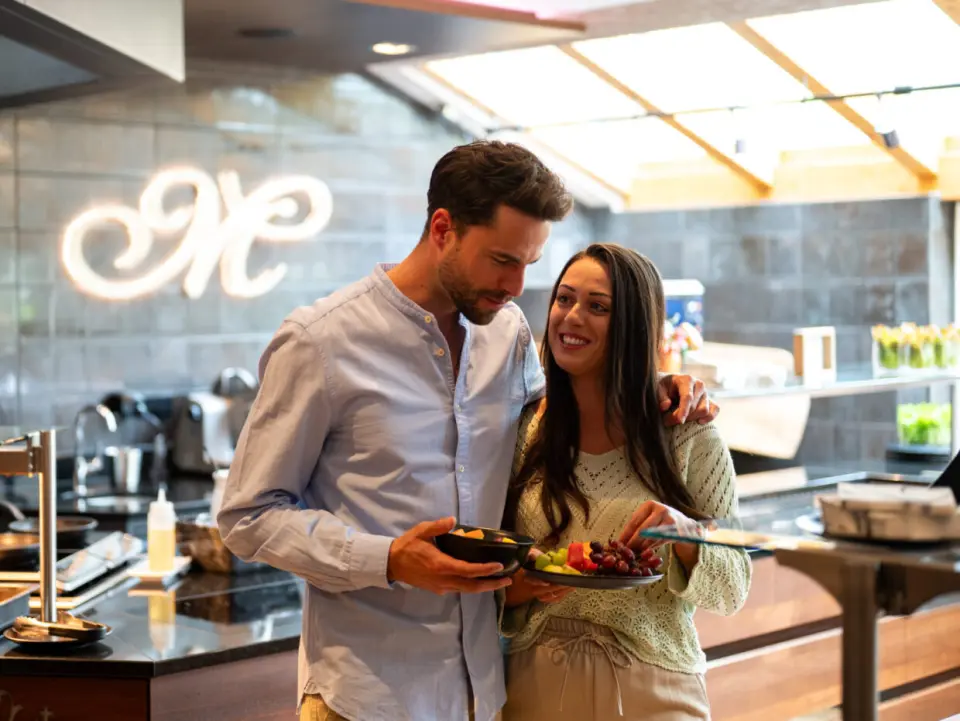 Glückliches Paar beim gesunden Frühstücksbuffet mit frischem Obst im modernen Restaurant des Meiser Vital Hotel.