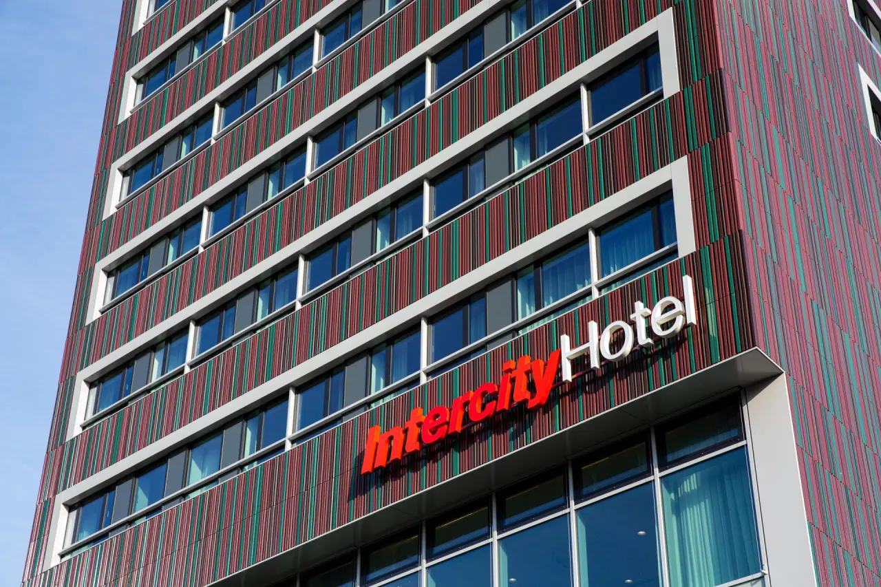 Moderne Fassade des Intercity Hotels mit markanten roten und grünen vertikalen Streifen unter klarem Himmel.