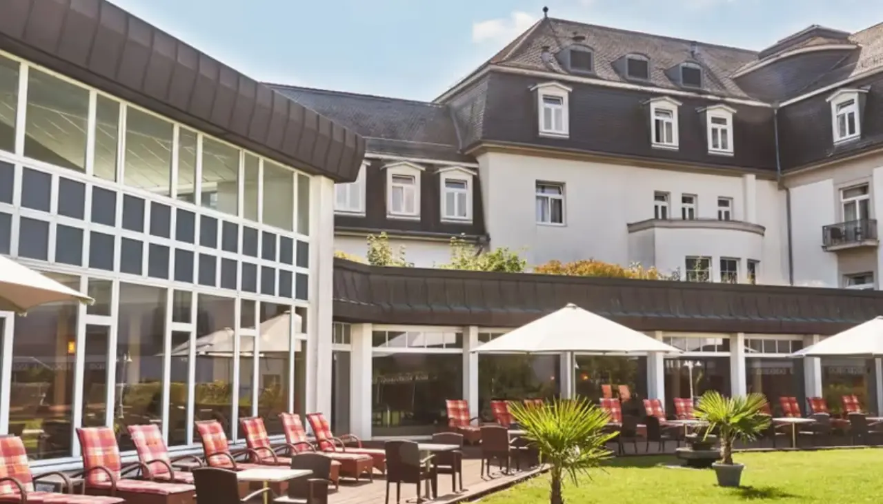 Aussenansicht des Steigenberger Hotel Bad Pyrmont mit moderner Glasfassade, Terrasse und Liegestühlen im Garten.