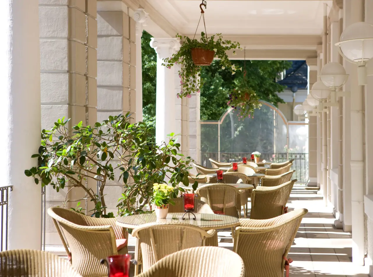 Einladende überdachte Terrasse mit Korbstühlen und Pflanzen im Steigenberger Bad Pyrmont, ideal für entspannte Stunden im Freien.