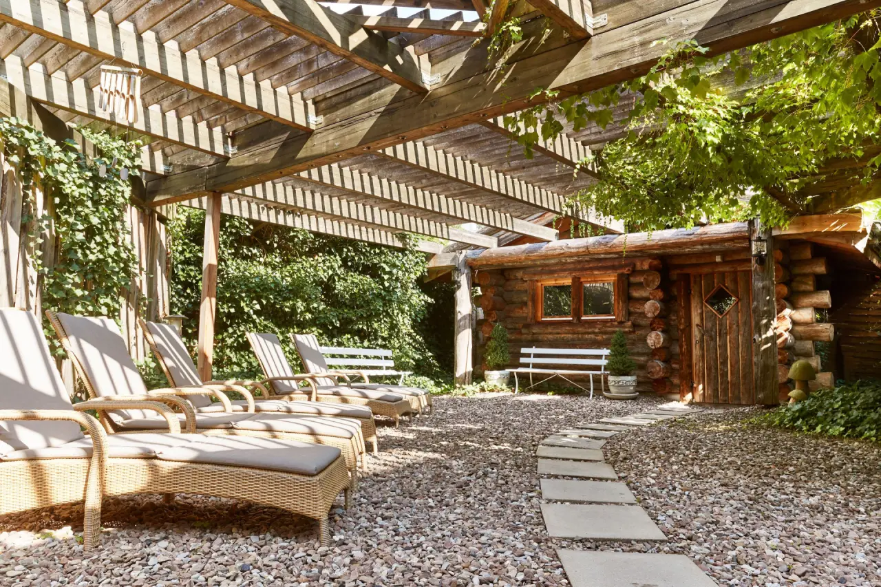 Entspannungsbereich mit Holzsauna und Sonnenliegen unter einer Pergola im Garten des Steigenberger Bad Pyrmont.