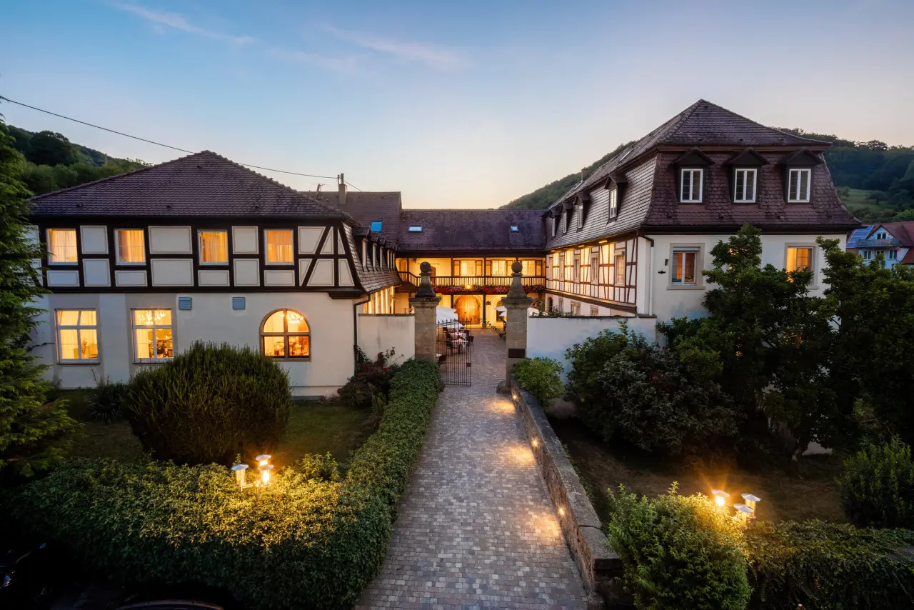 Romantische Aussenansicht des Schloss Döttingen bei Sonnenuntergang mit beleuchteten Fenstern und Gartenweg.