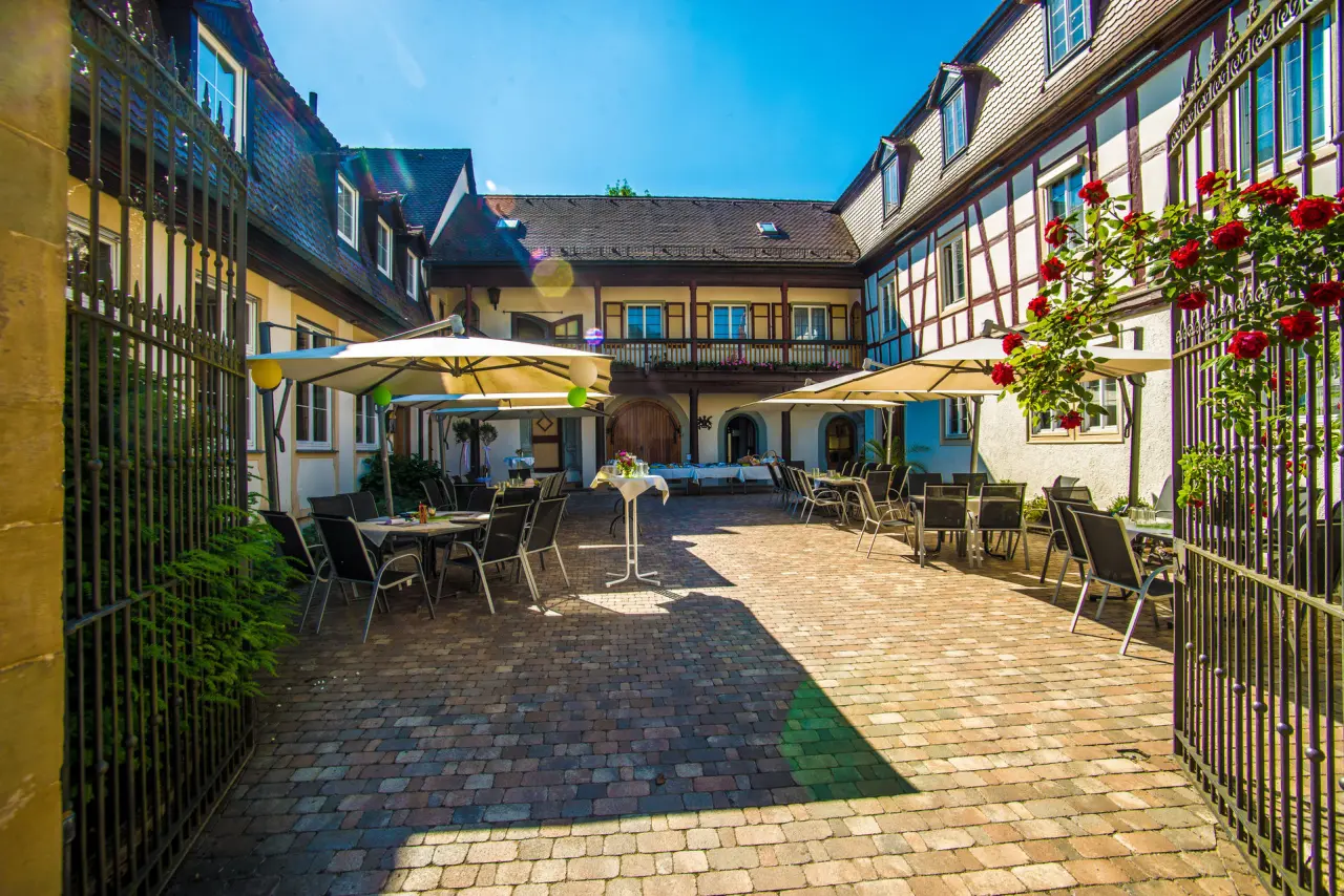 Historischer Innenhof von Schloss Döttingen mit Tischen, Sonnenschirmen und Rosenranken für entspannte Stunden im Freien.