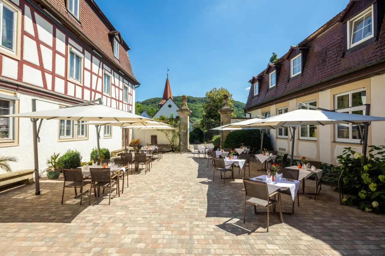 Sonniger Restaurant-Aussenbereich im Innenhof von Schloss Döttingen mit Fachwerkhäusern und Blick auf die Kirche.