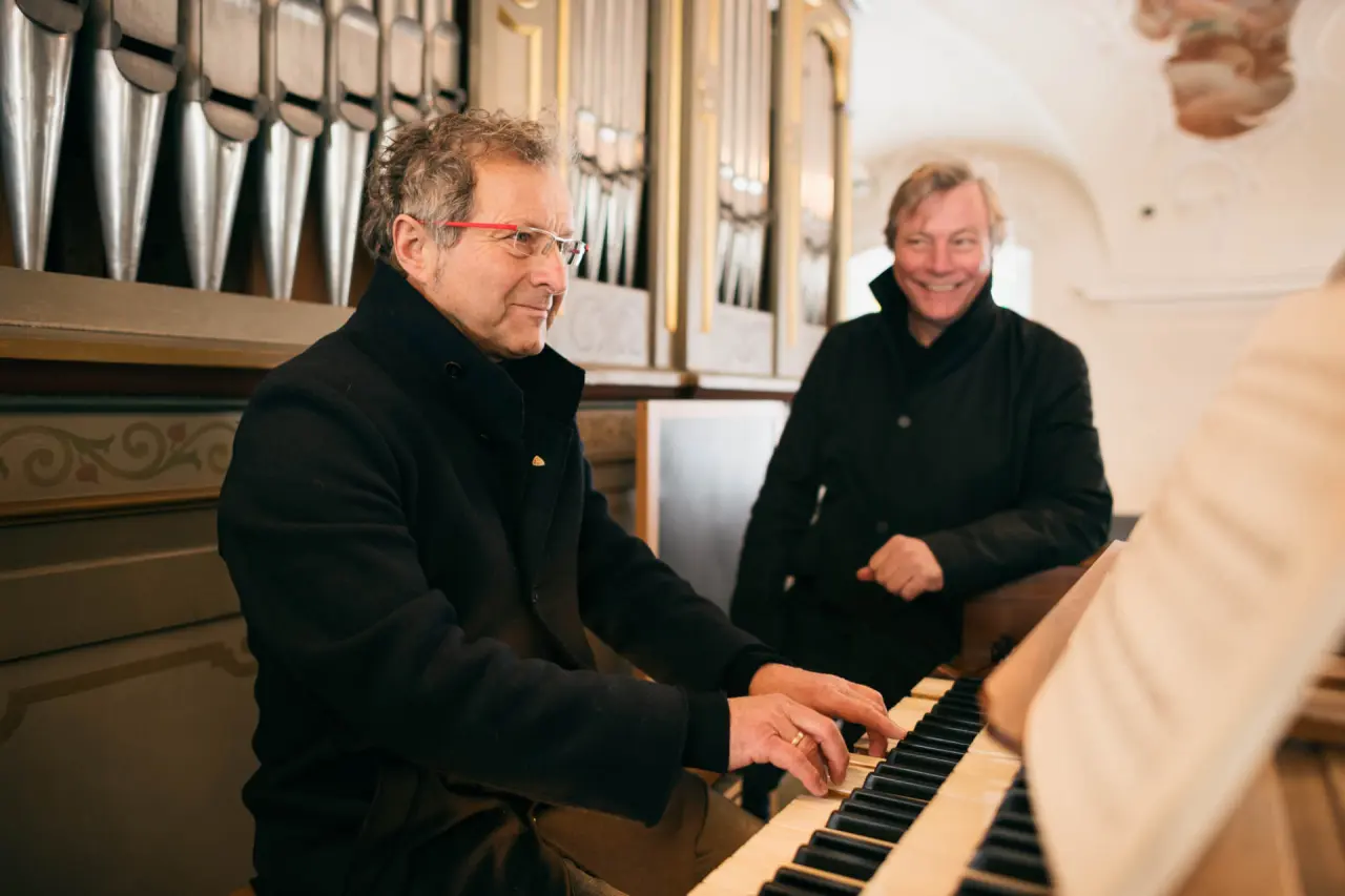Zwei Männer an einer historischen Kirchenorgel, einer spielt, der andere lächelt, im Hotel Krone Au - DAS BREGENZERWALDHOTEL.