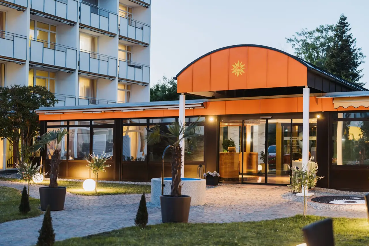 Einladende Abendansicht des Kurhotel Sonnenhof mit beleuchtetem Eingang, oranger Fassade und Gartenbeleuchtung.